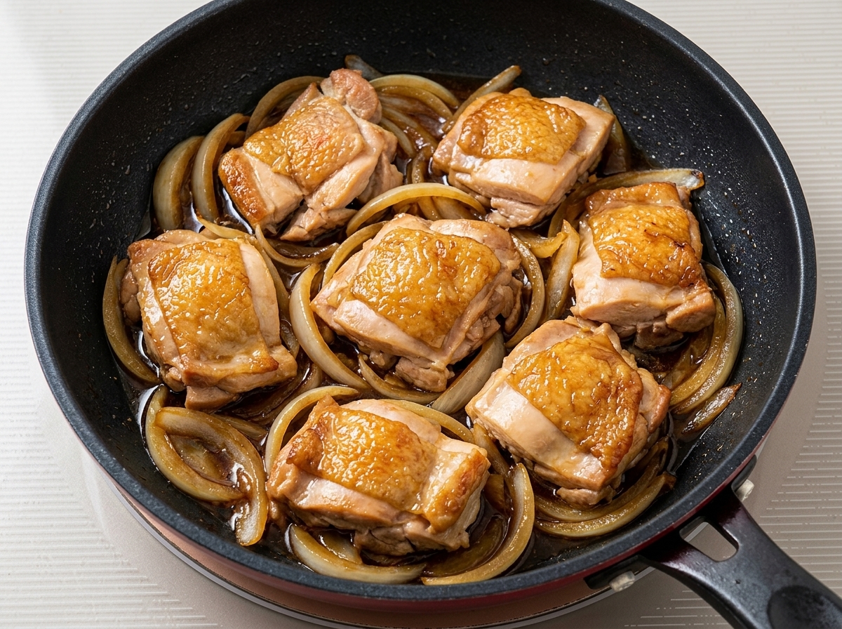 Pezzi di pollo fritto che sobbollono con cipolle e salsa scura in una padella.