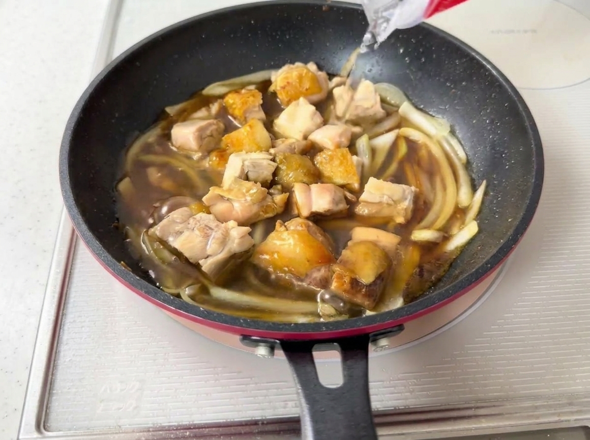 Acqua versata in una padella contenente pollo in ebollizione, cipolle e salsa scura.