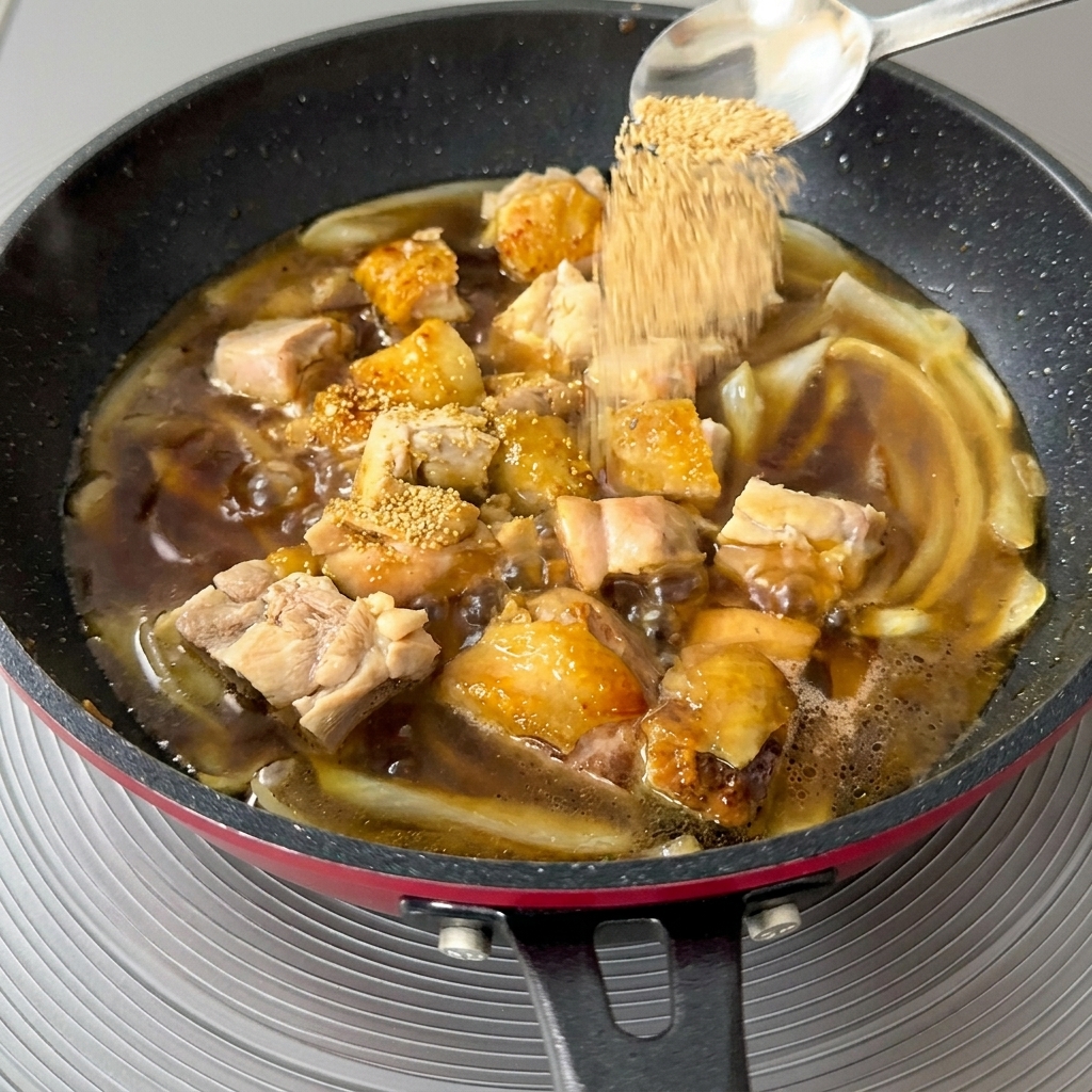 Primo piano di un cucchiaio di granuli di dashi dorati sparsi in una padella in ebollizione con pollo e cipolle.