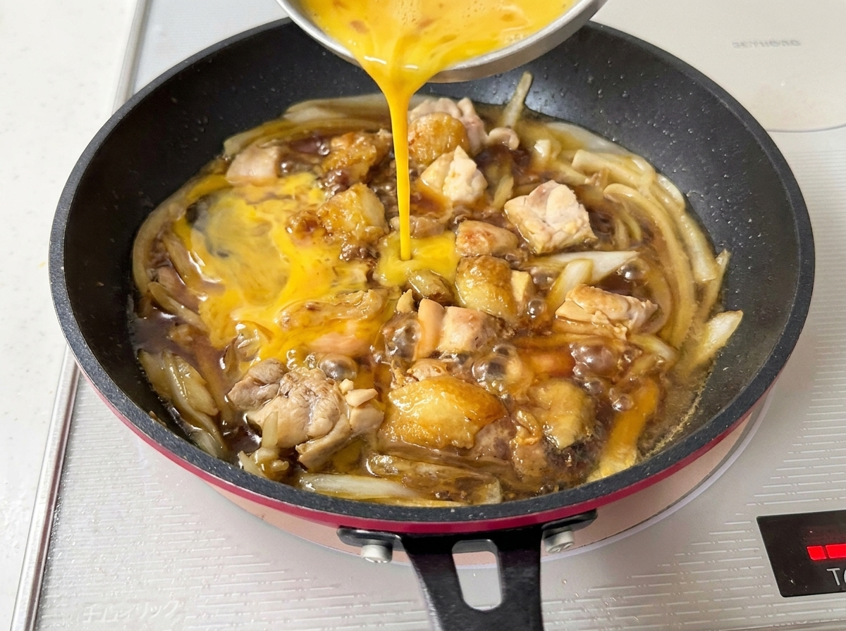 Uova sbattute versate da una ciotola nella padella, coprendo il pollo e le cipolle in ebollizione.