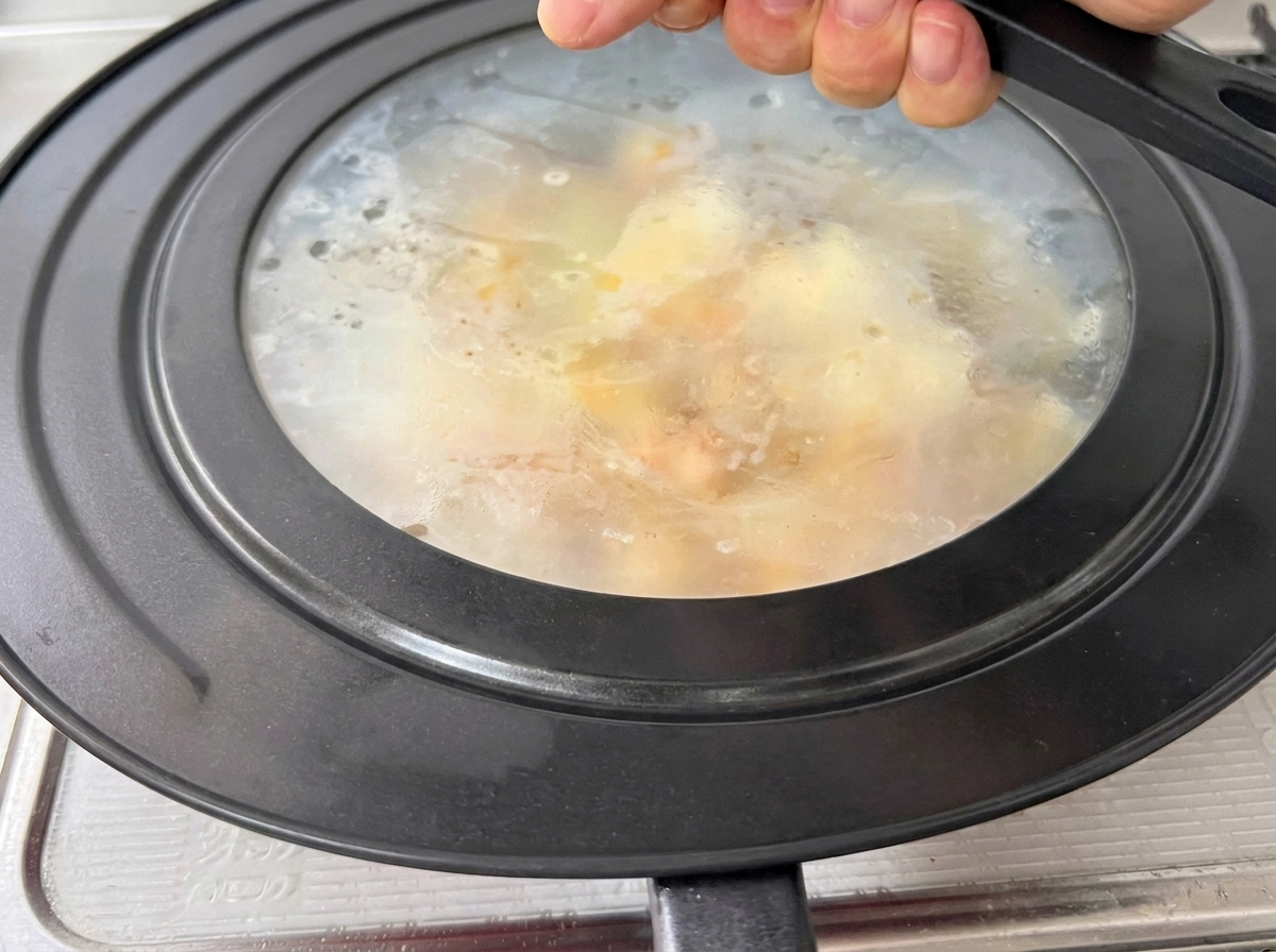 Un coperchio di vetro posizionato su una padella rossa, con vapore visibile allinterno.