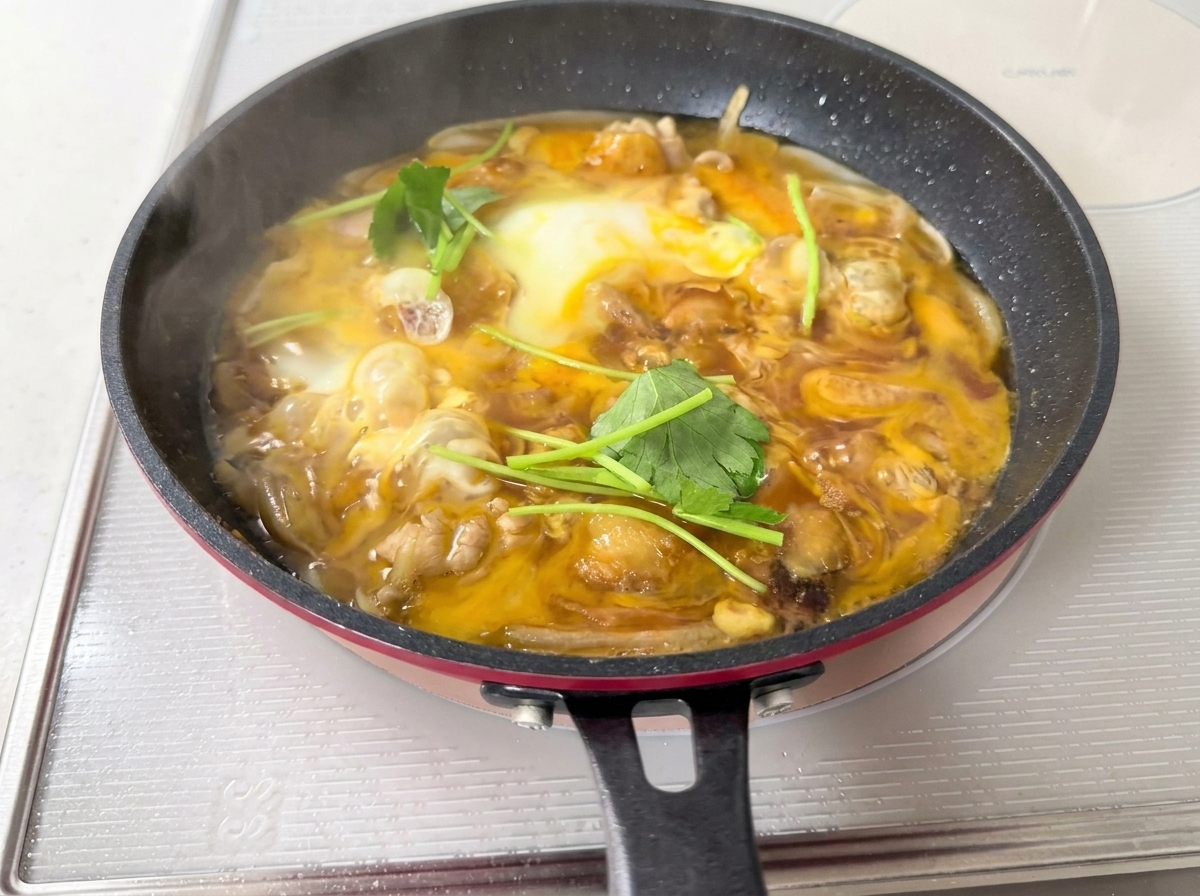 Foglie di mitsuba verdi fresche sparse sopra una padella di uovo morbido e pollo.