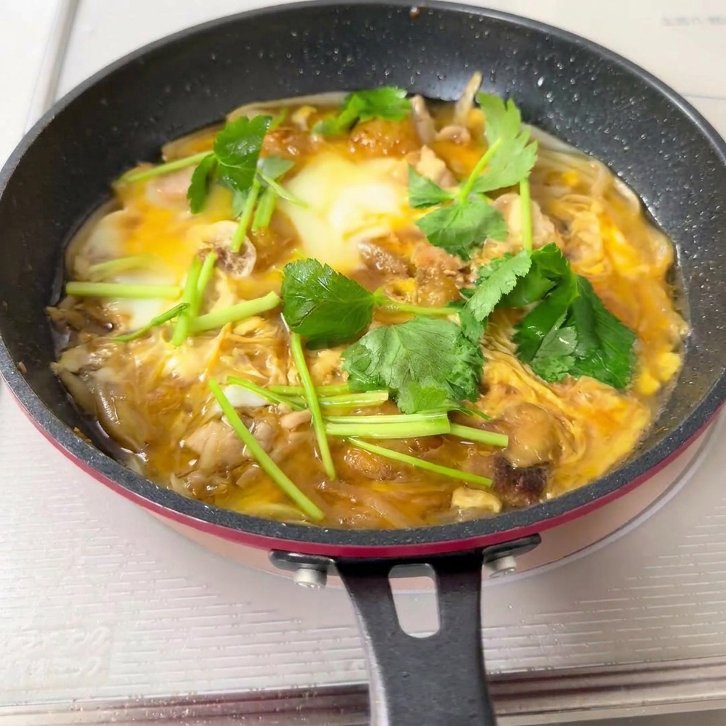 Una padella piena di composto di Oyakodon cotto versato sopra una ciotola di riso bianco.