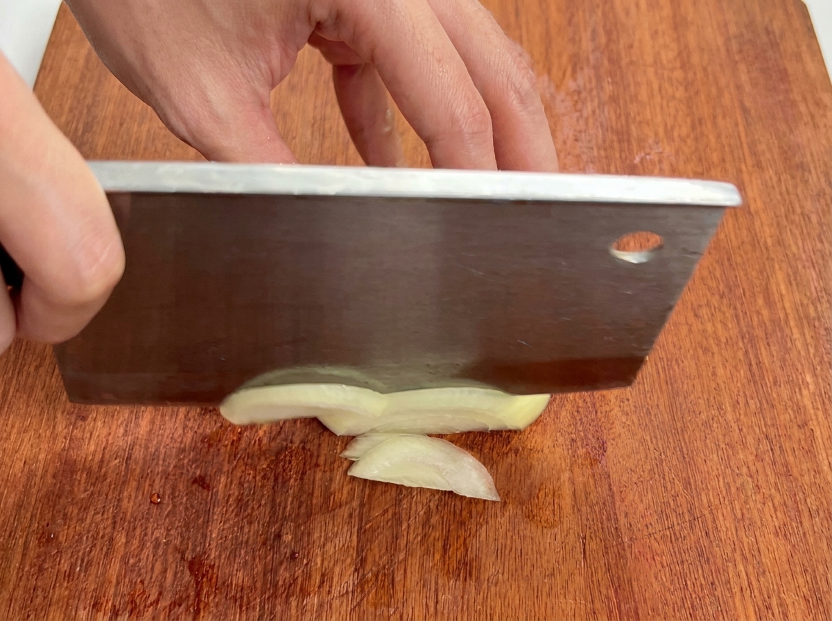 Vista ravvicinata di una cipolla bianca tagliata a strisce sottili su un tagliere di legno.