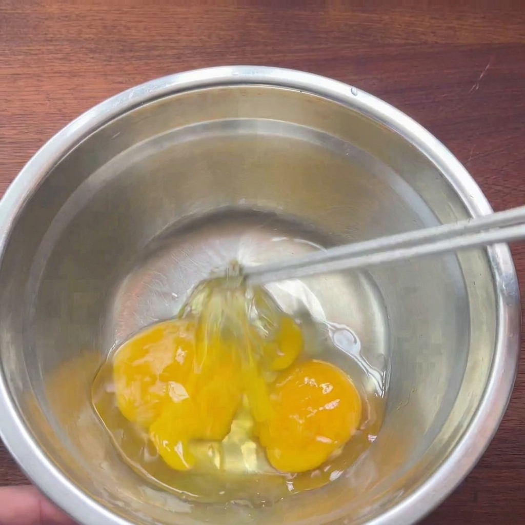 Due uova crude in una ciotola di metallo sbattute leggermente con le bacchette.