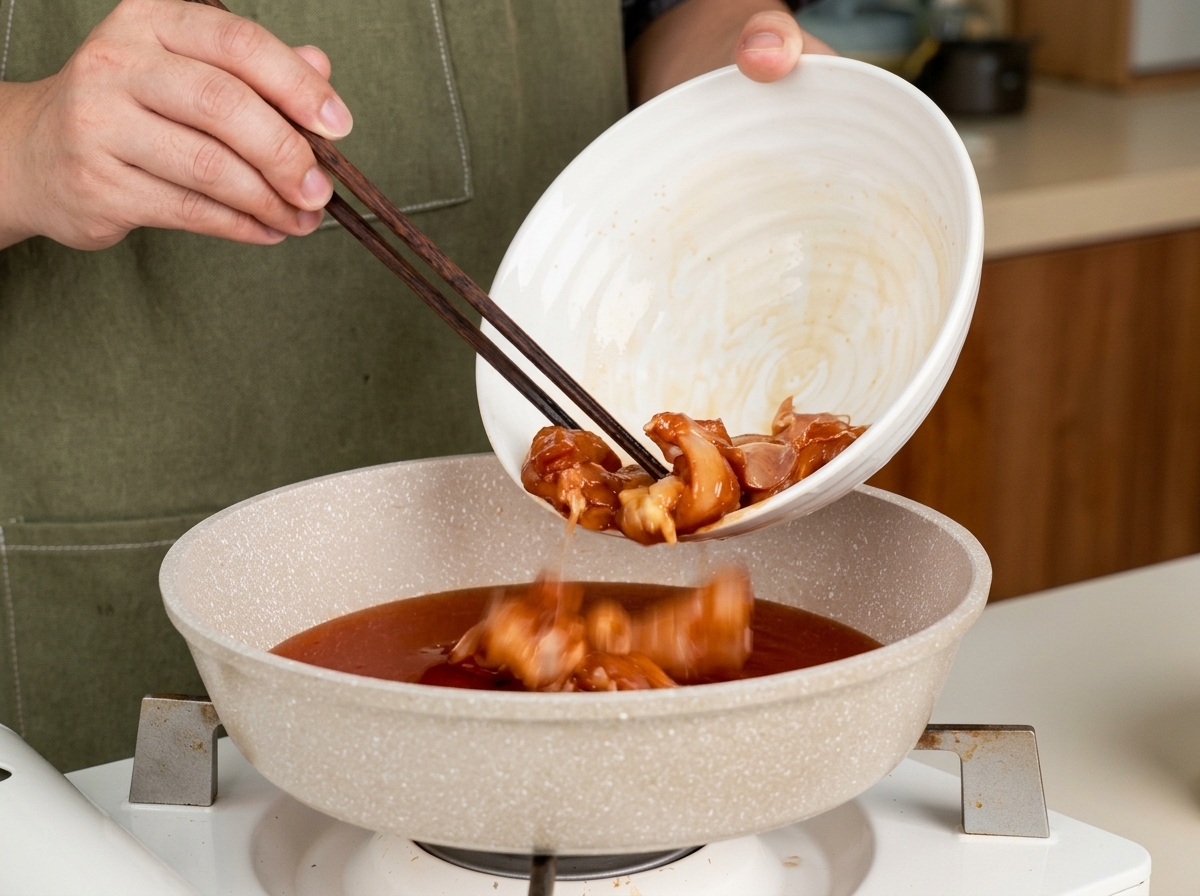 Pezzi di pollo aggiunti a una padella con salsa teriyaki usando delle bacchette.