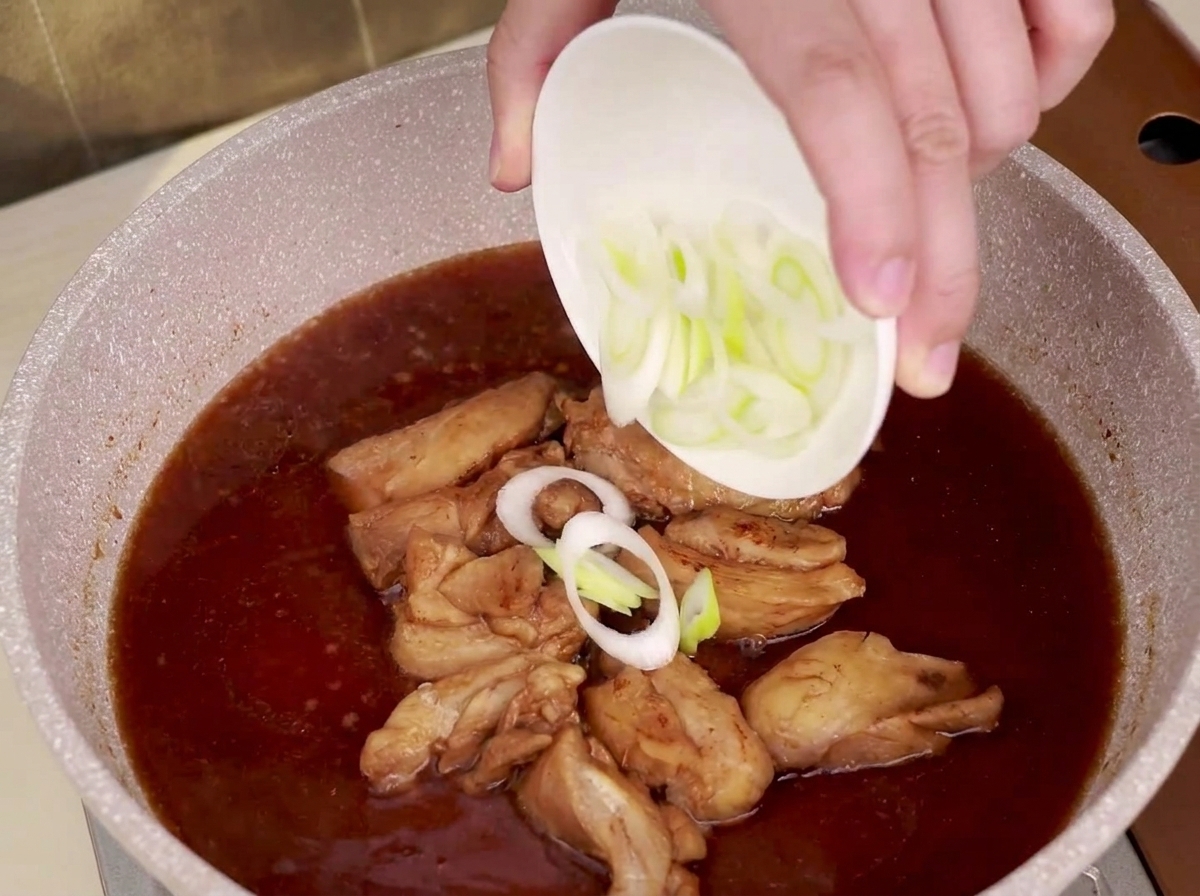 Porro a fettine cosparso su una padella con pollo a fuoco lento e salsa teriyaki.