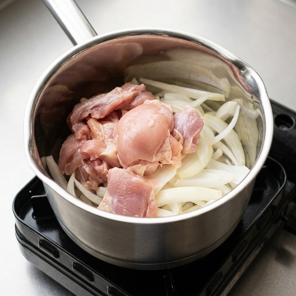 Cipolle e pezzi di pollo in una pentola, conditi con i condimenti liquidi.