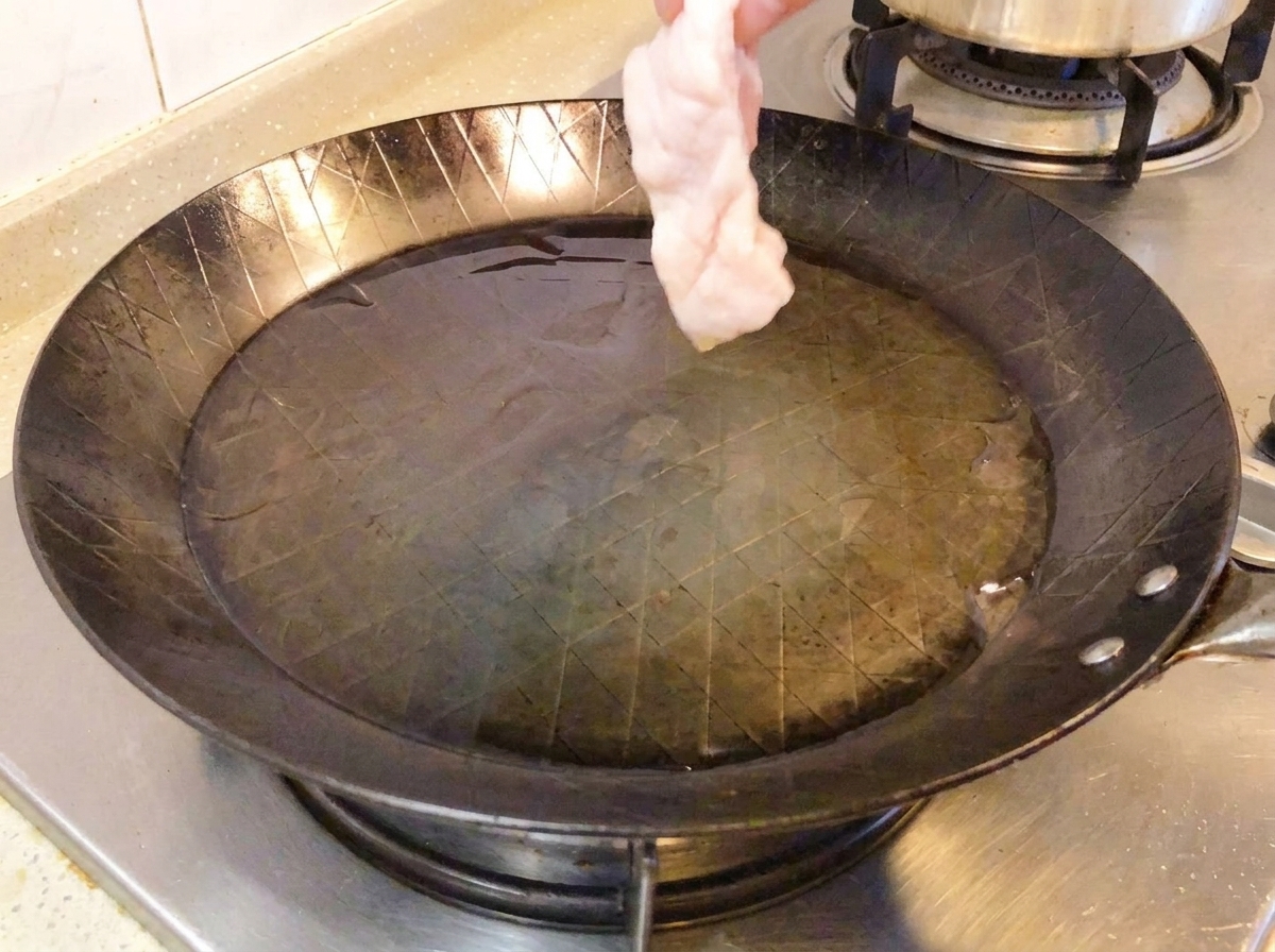 Coscia di pollo cruda posizionata dal lato della pelle in una padella calda.