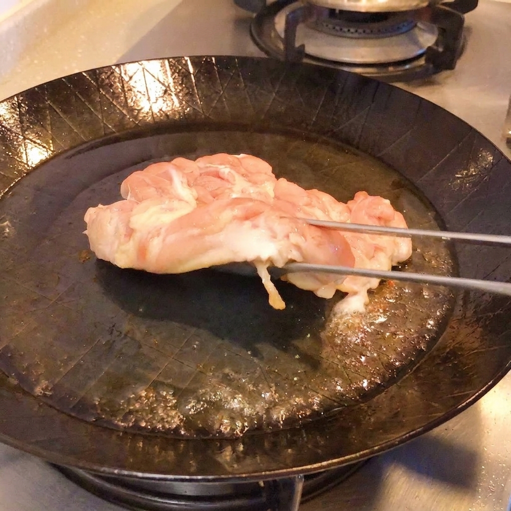 Pinze che sollevano il pollo in padella per mostrare la pelle croccante e dorata.