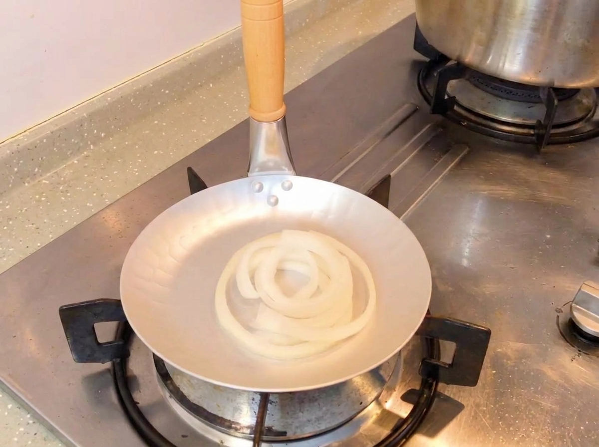 La miscela di salsa di soia scura viene versata da un cucchiaio in una padella contenente anelli di cipolla bianca cruda.