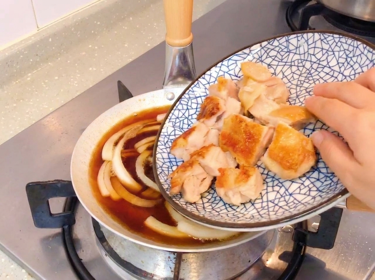 Fette di pollo croccante cotto in padella aggiunte a una padella con cipolle a fuoco lento e salsa a base di soia.
