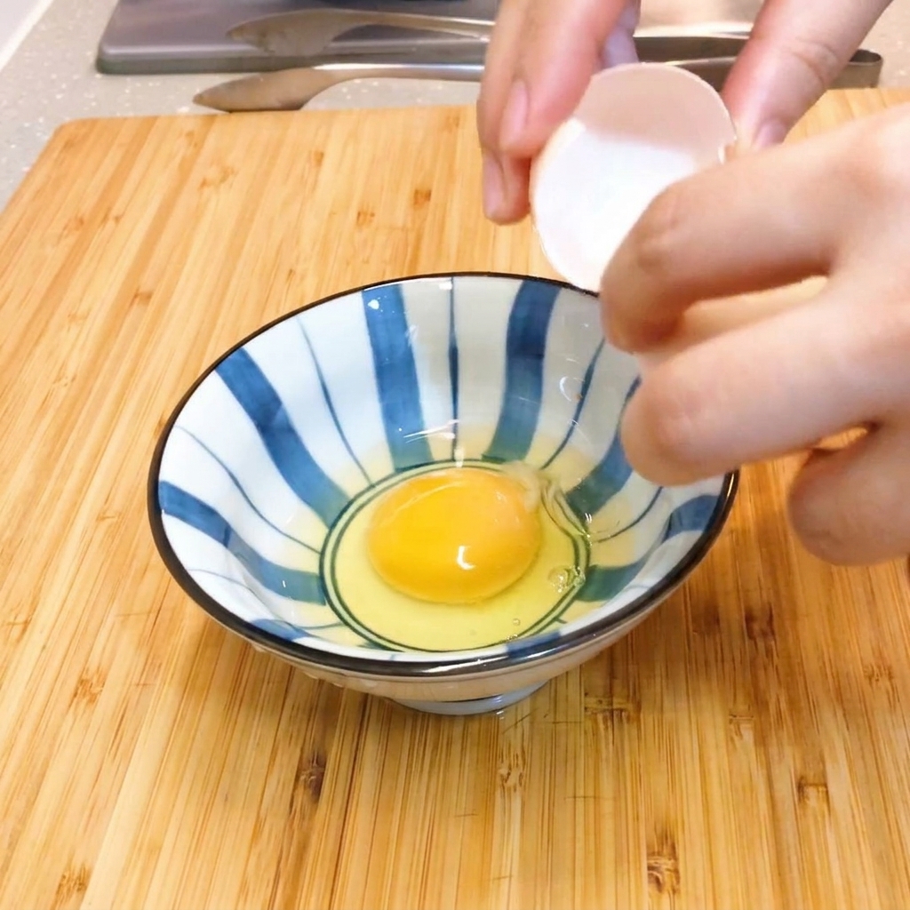 Due uova crude mescolate delicatamente con le bacchette in una ciotola di ceramica a strisce blu e bianche.