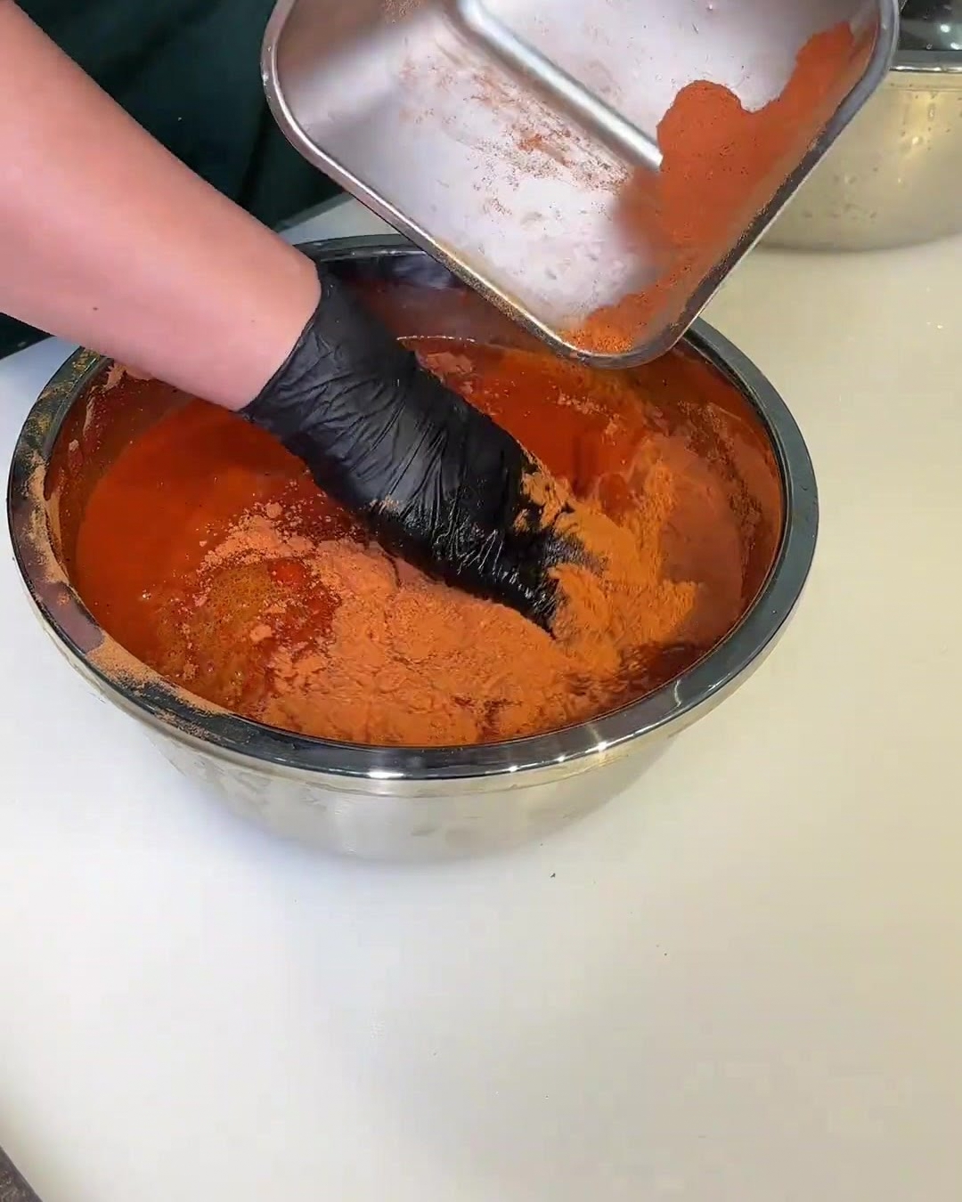 Ciotola con salsa marinata rossa in cui una mano guantata mescola le fette di maiale.