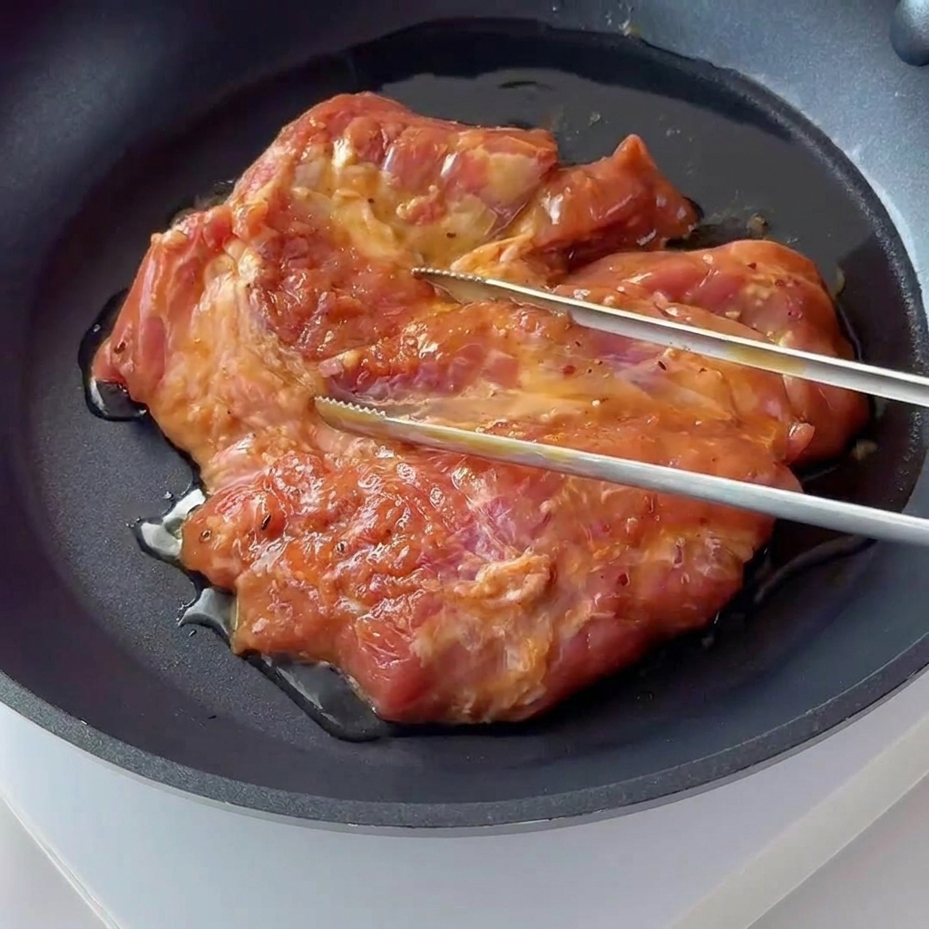 Una braciola condita sfrigola e si dora in una padella antiaderente scura.
