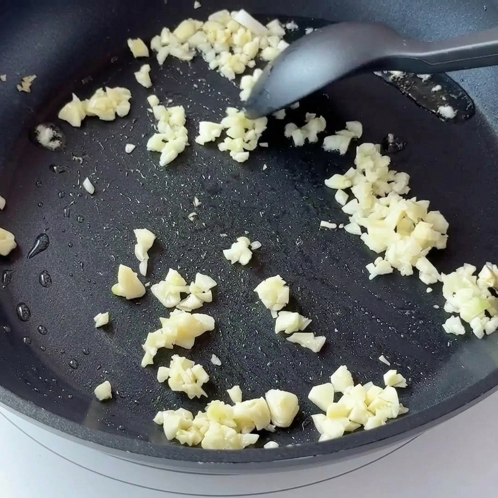 Aglio tritato e cipolla a dadini che friggono in una padella antiaderente.