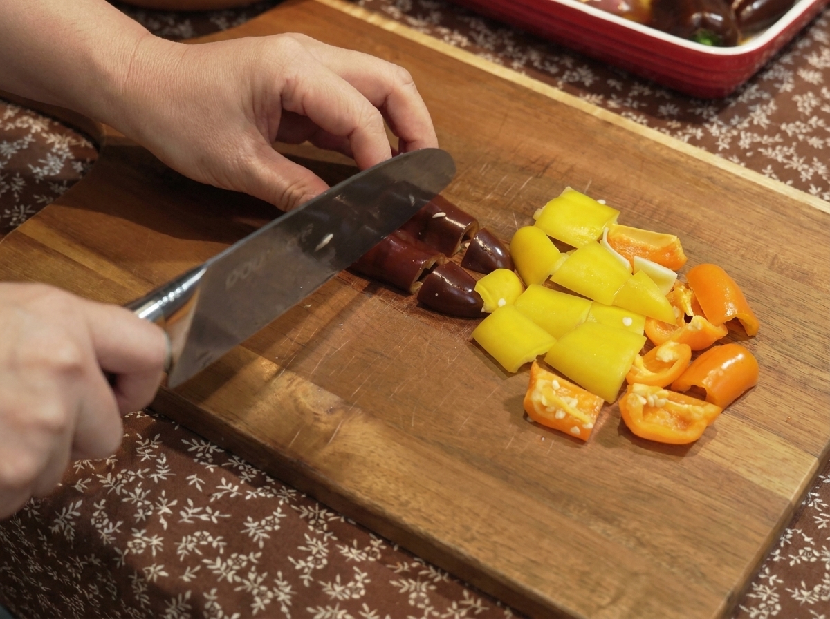Peperoni e cipolle tagliati a pezzetti su un tagliere di legno.
