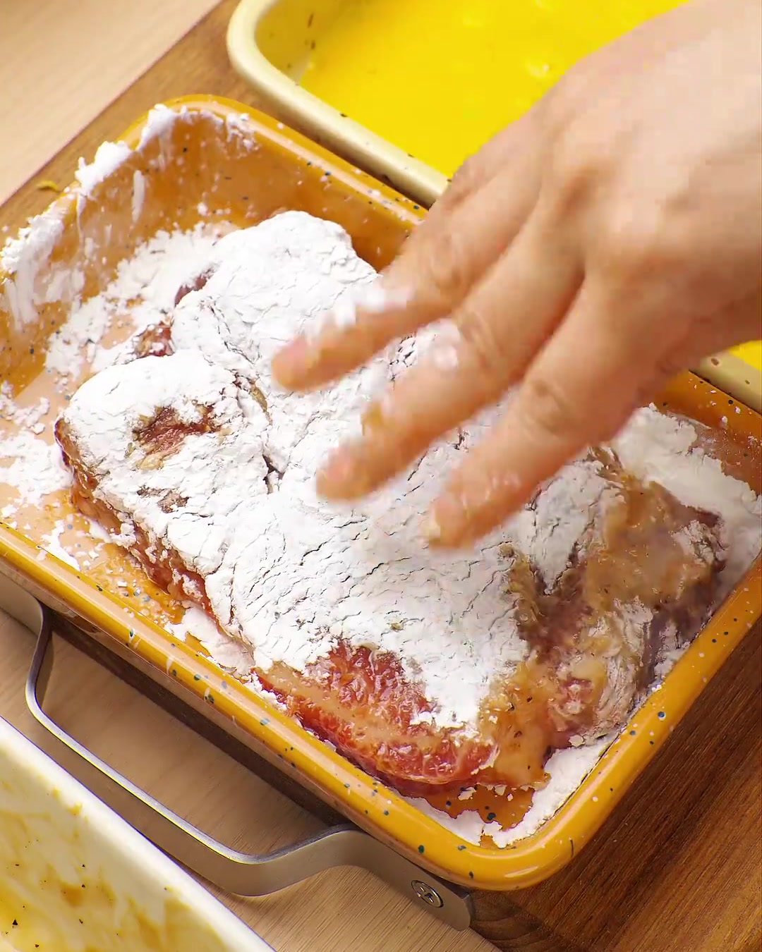 Una mano preme una cotoletta passata nelluovo in un vassoio di panko, assicurando una copertura completa.