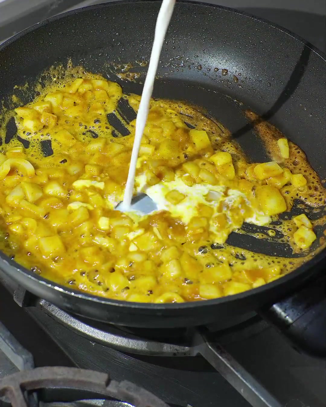 Latte di cocco versato in una padella con curry sciolto e cipolle saltate, creando una salsa gialla cremosa.