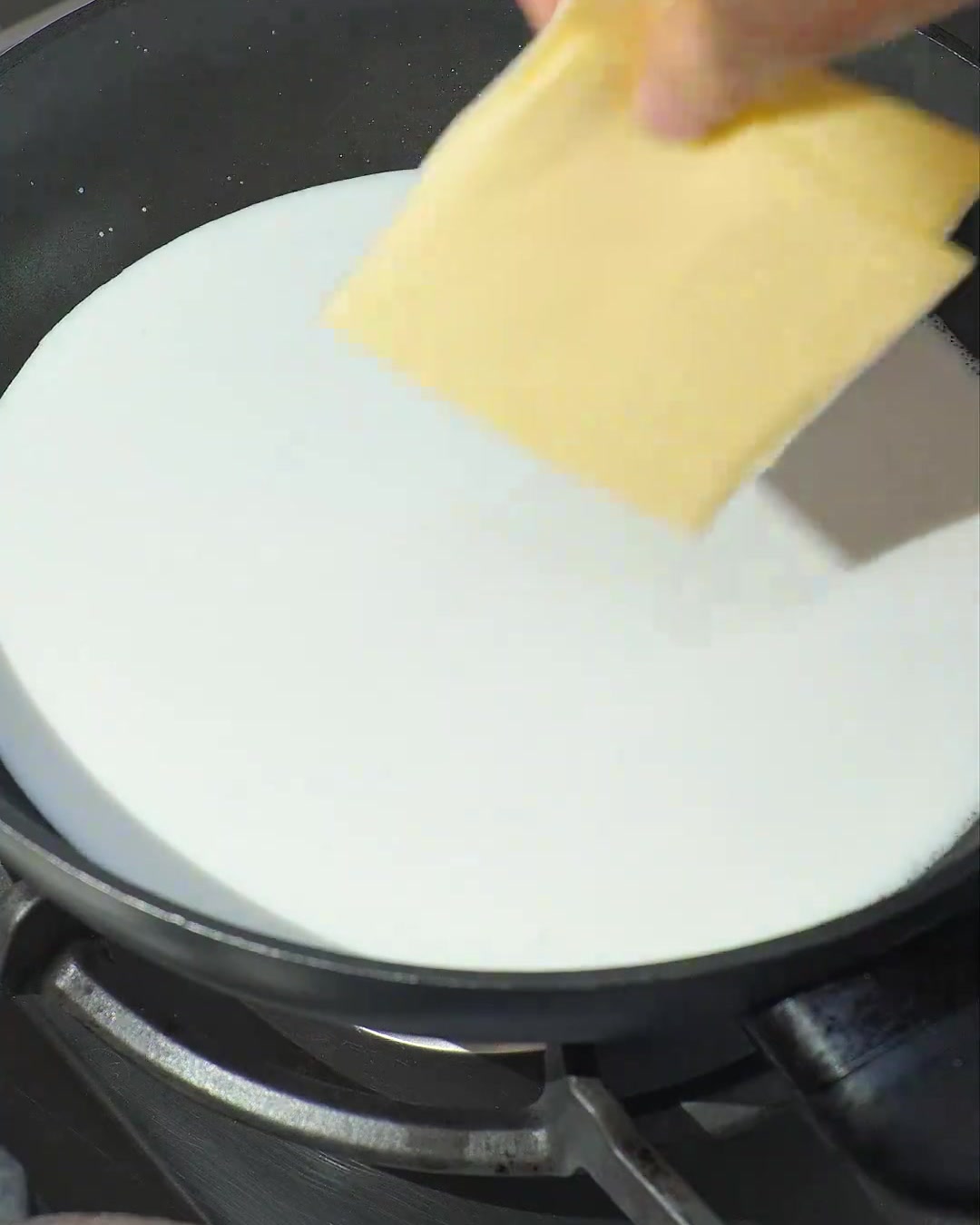Due fette di formaggio giallo che fondono in latte di cocco bianco in ebollizione in una padella scura.