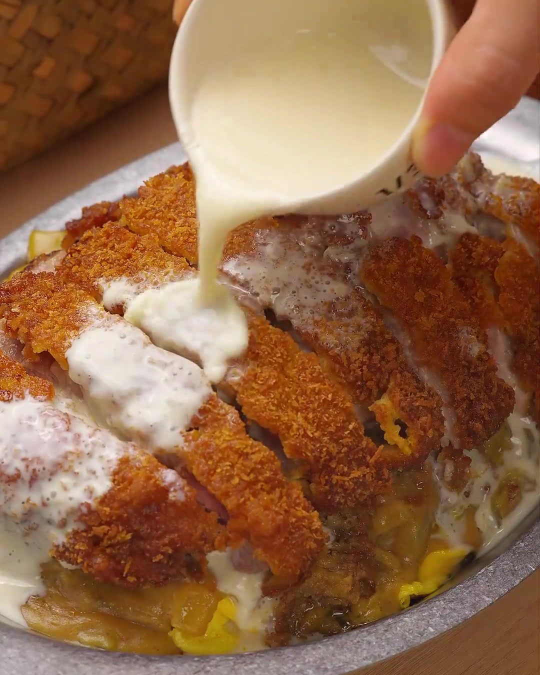 Un primo piano di una salsa bianca e cremosa al formaggio e cocco versata sopra cotolette di maiale a fette dorate, guarnita con prezzemolo verde fresco.
