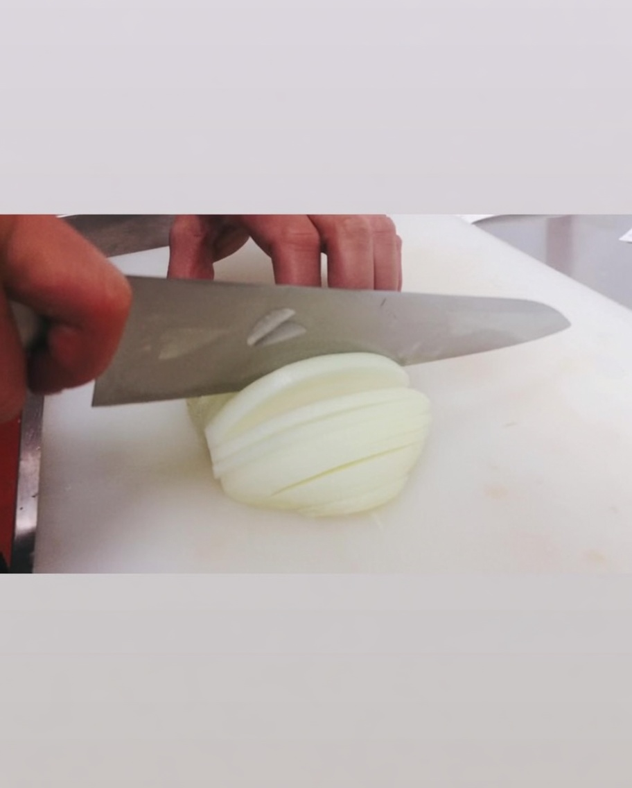 Affettare una cipolla bianca su un tagliere bianco.
