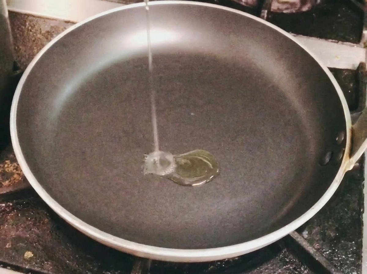 Olio versato in una padella nera su fornello.