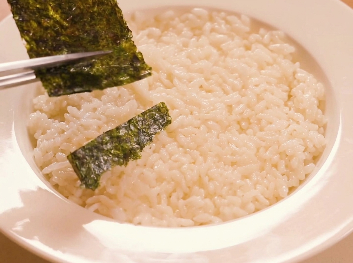 Strisce di alga nori tostata disposte con cura sul letto di riso condito usando le bacchette.