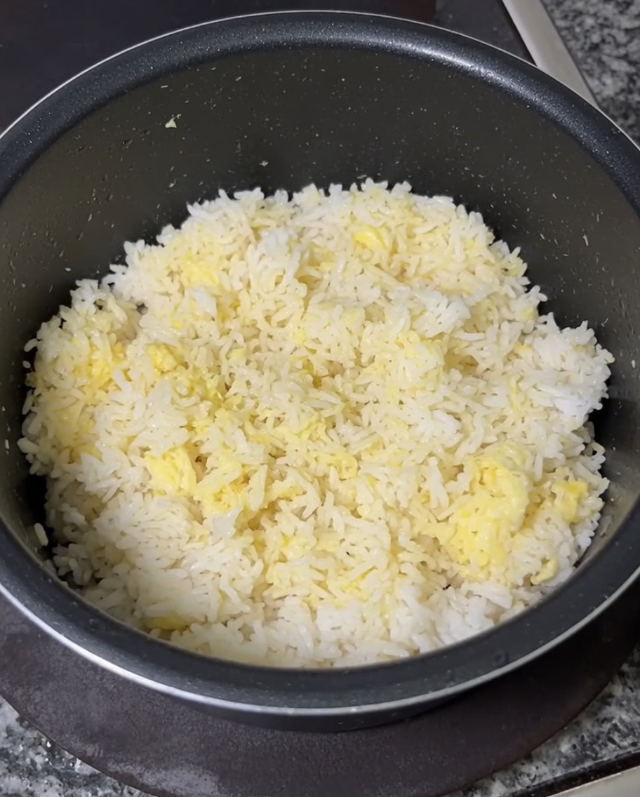 Una mano mescola i tuorli duovo nel riso freddo fino a renderlo giallo.