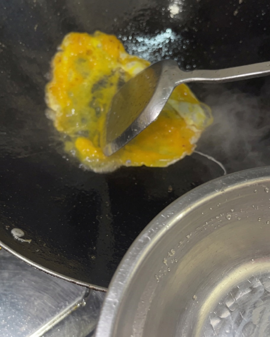 Versare uova sbattute in un wok caldo con verdure e carne.