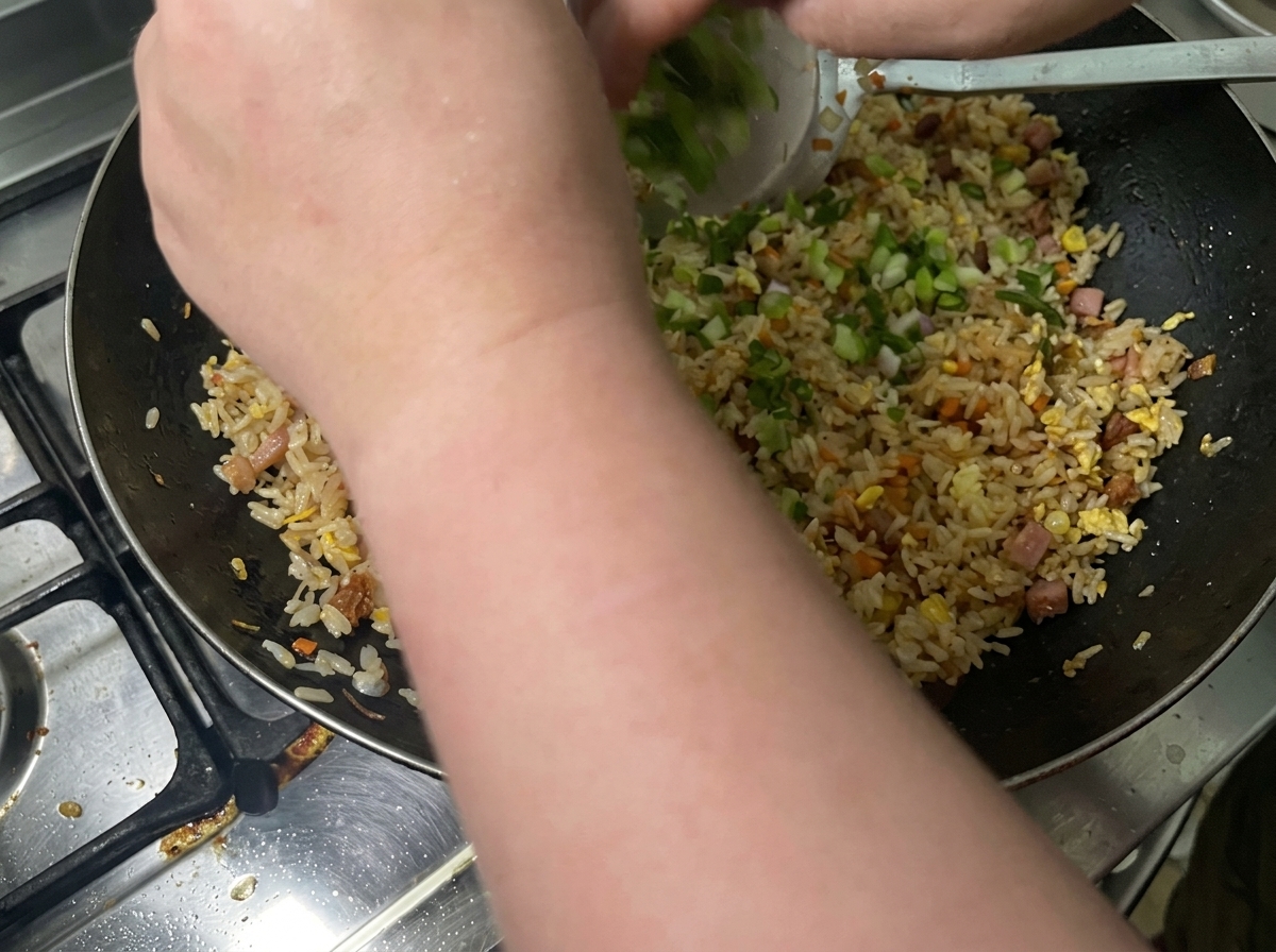 Cipollotti tritati aggiunti nel wok con il riso.