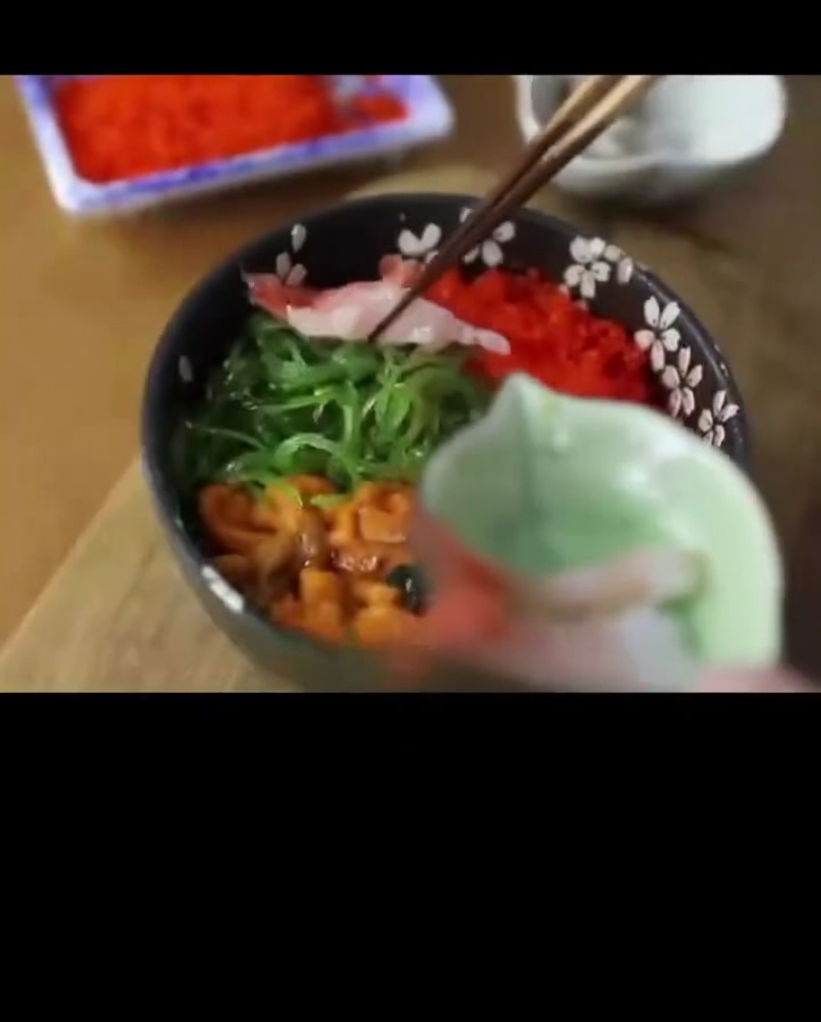Gamberi dolci crudi e traslucidi posizionati sul bordo di una ciotola di riso ai frutti di mare.