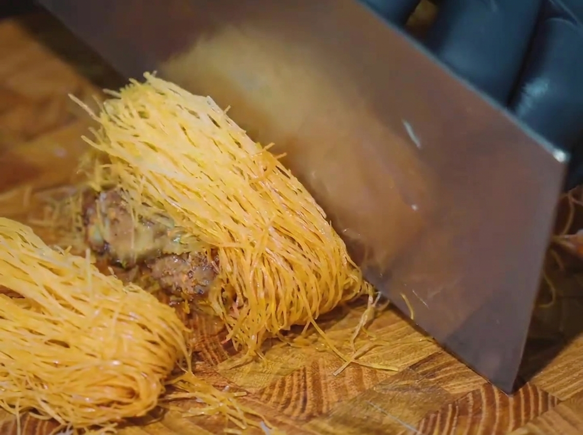 Una mannaia che affetta un rotolo di manzo dorato su un tagliere di legno.