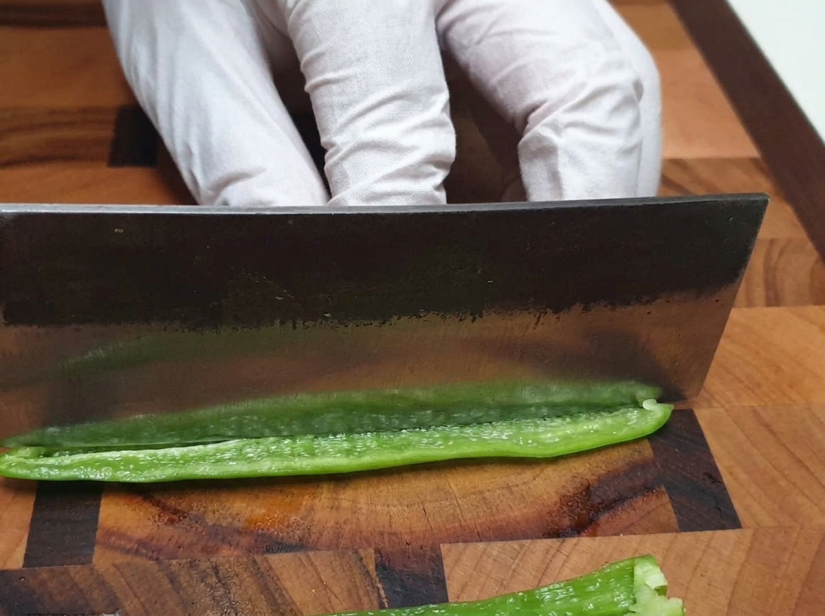 Un coltello da chef che trita finemente un peperoncino verde su un tagliere di legno.