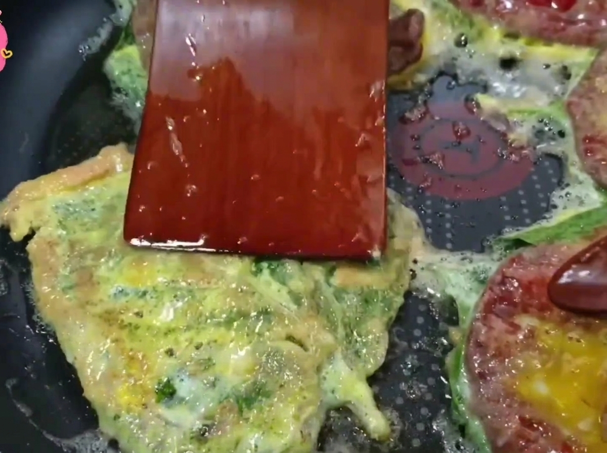 Una spatola di legno che capovolge una frittella di manzo dorata in una padella rovente.