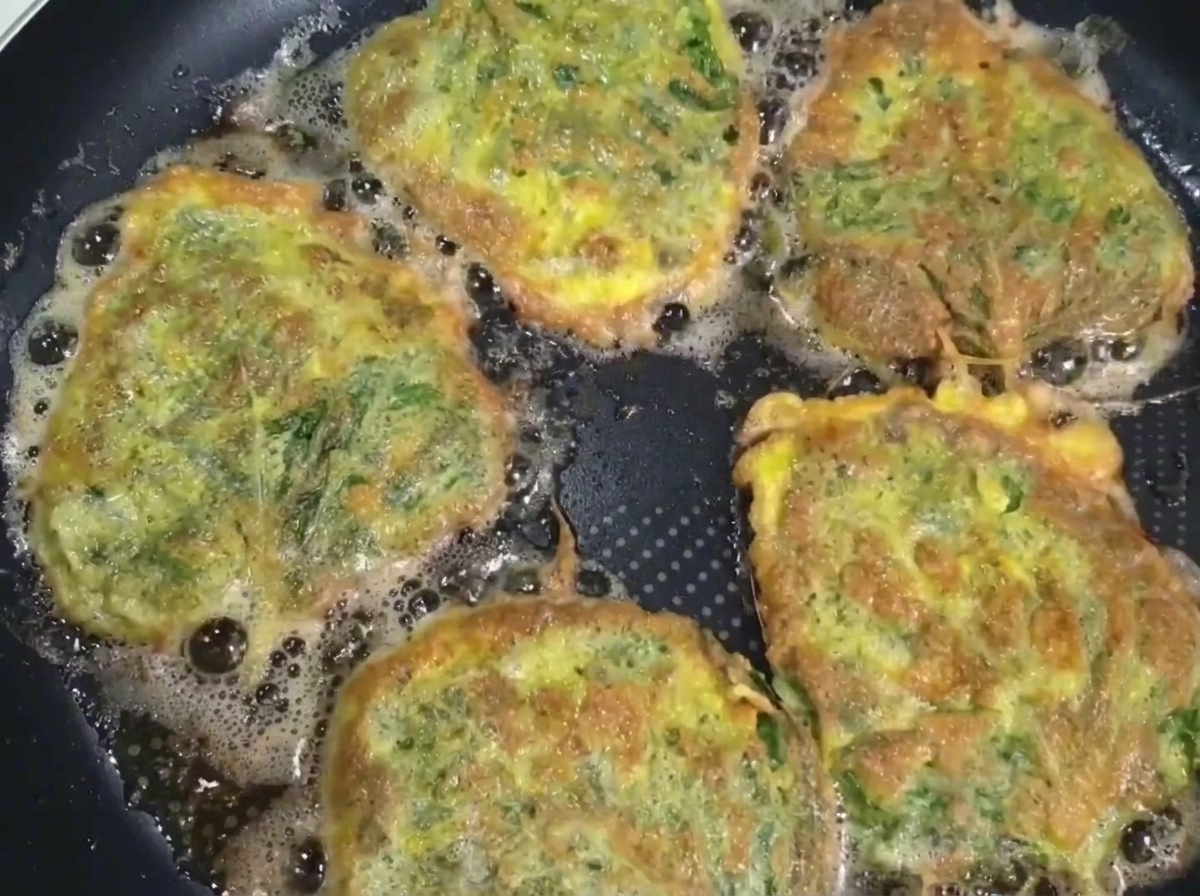Una frittella di manzo e perilla cotta, sollevata dalla padella con una spatola e delle bacchette.