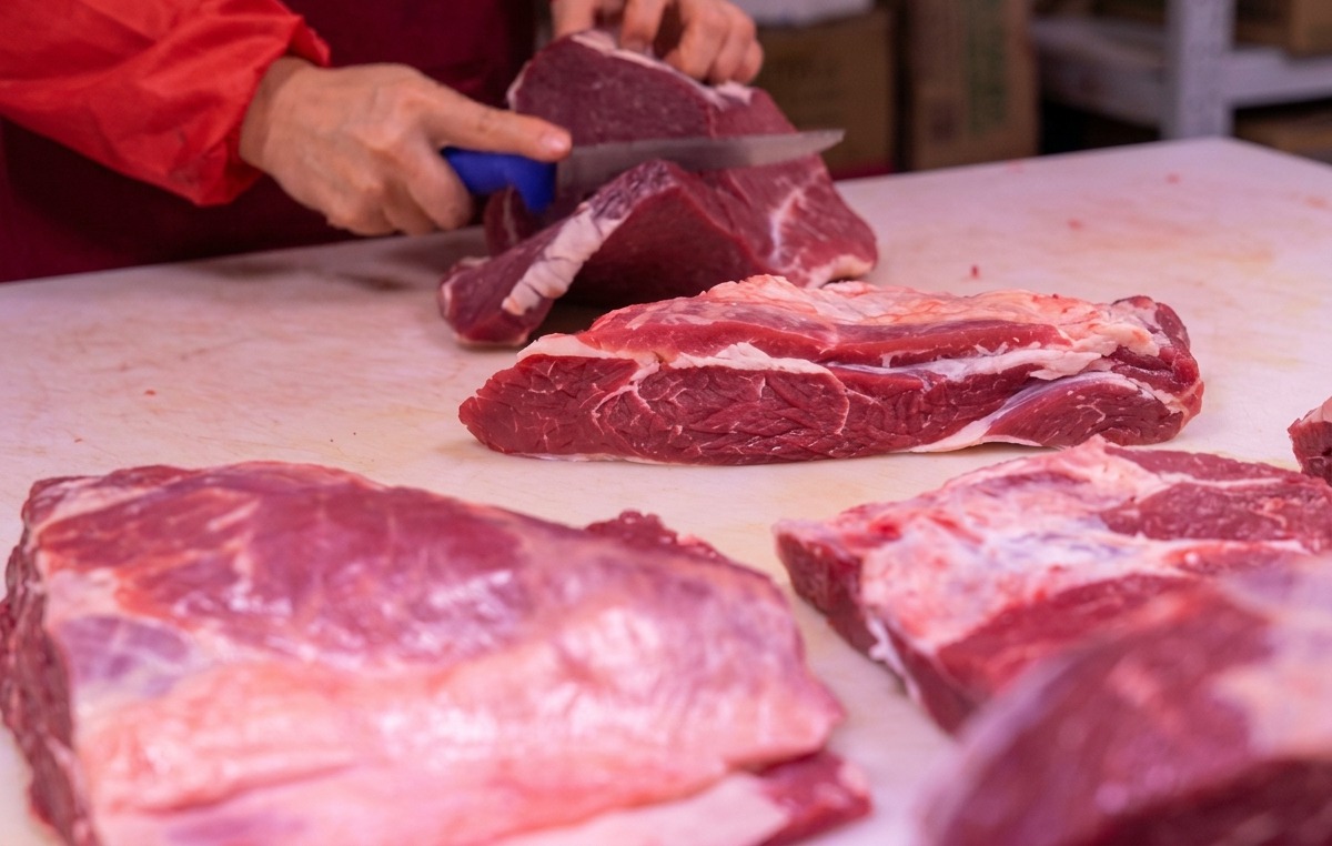 Mani che usano un coltello affilato per affettare carne rossa su un tagliere bianco.