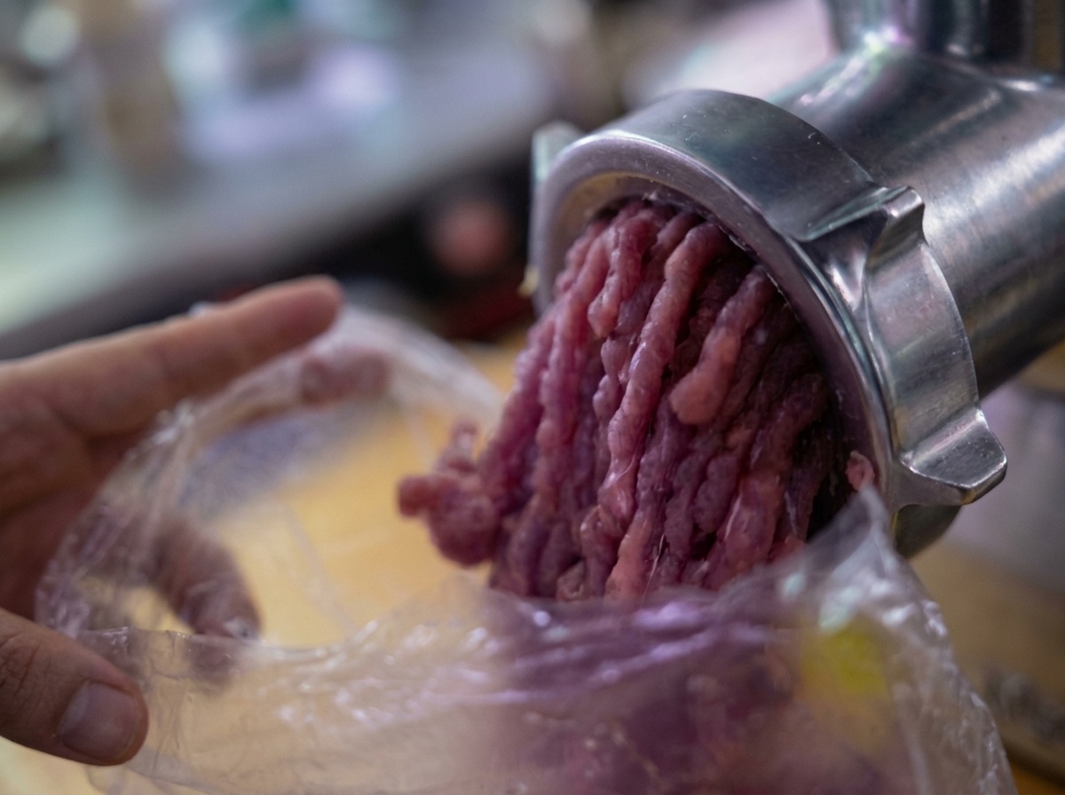 Carne macinata che esce da un tritacarne meccanico in un sacchetto di plastica.