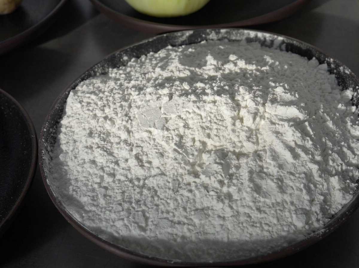 Salsa di soia versata in una grande ciotola di metallo contenente carne macinata, amido bianco e condimenti.