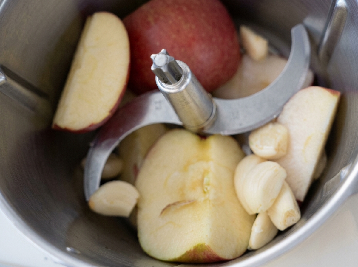 Fette di mela e spicchi daglio sbucciati allinterno di un robot da cucina prima di frullare.