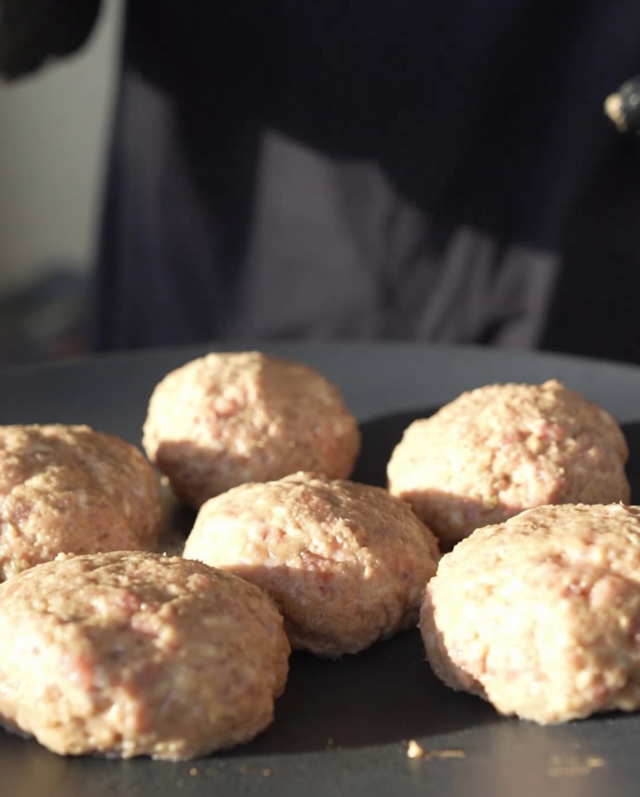 Polpette di carne rotonde che cuociono su una piastra nera in ghisa a fuoco basso.