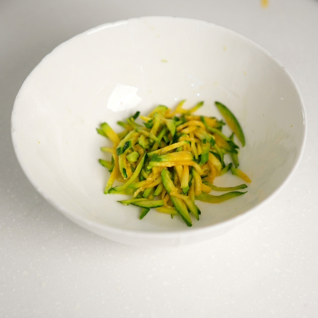 Carne macinata fresca aggiunta alla ciotola contenente le strisce di zucchine scolate.