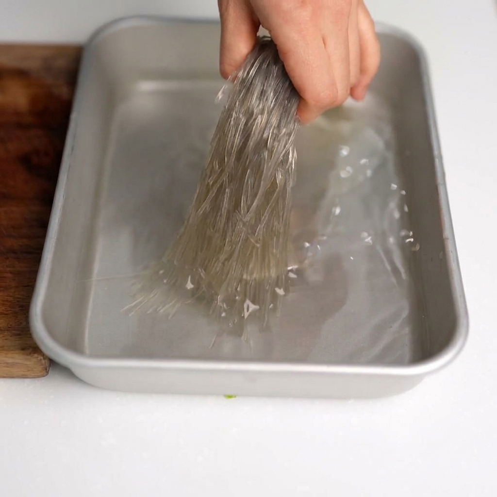 Forbici da cucina che tagliano a pezzetti gli spaghetti di soia precedentemente ammorbiditi in una ciotola.