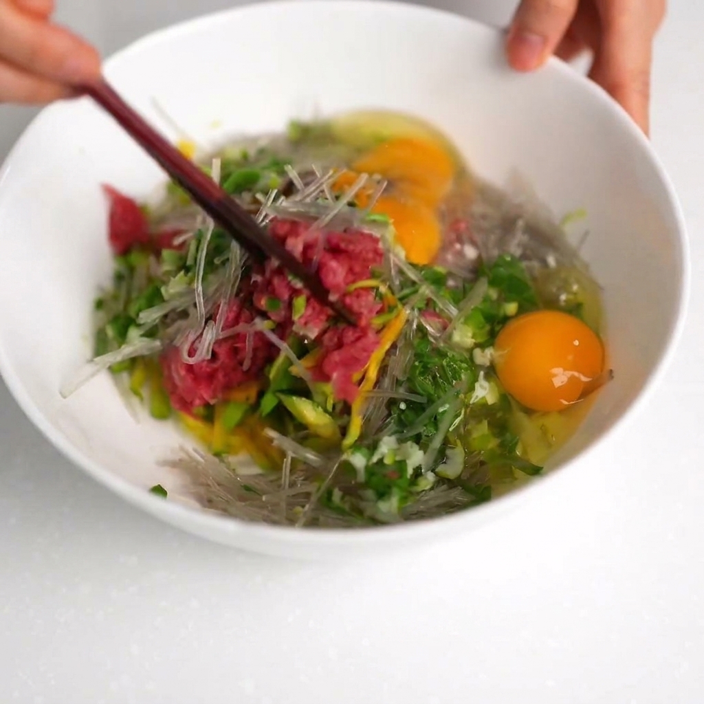 Un mix di manzo, zucchine e spaghetti di soia mescolato con le bacchette in una ciotola bianca.