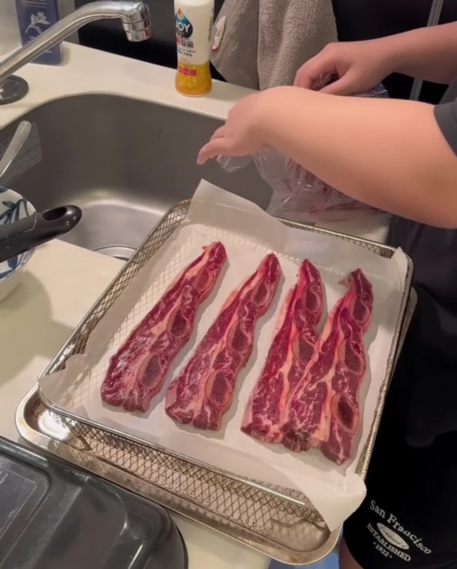 Primo piano di mani che usano carta assorbente per tamponare delle costine di manzo crude e assorbire lumidità superficiale.