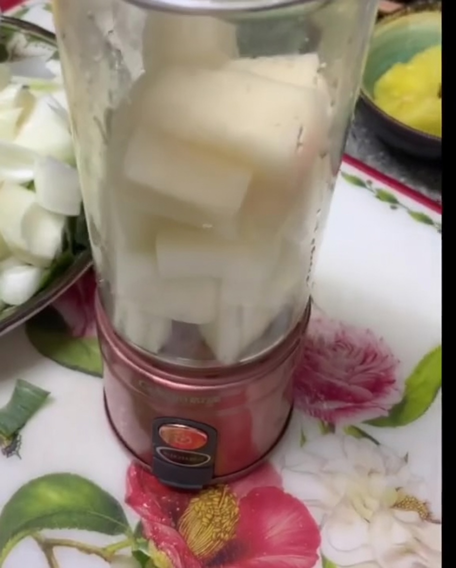 Pezzi di pera bianca e cipolla impilati allinterno della caraffa trasparente di un frullatore.