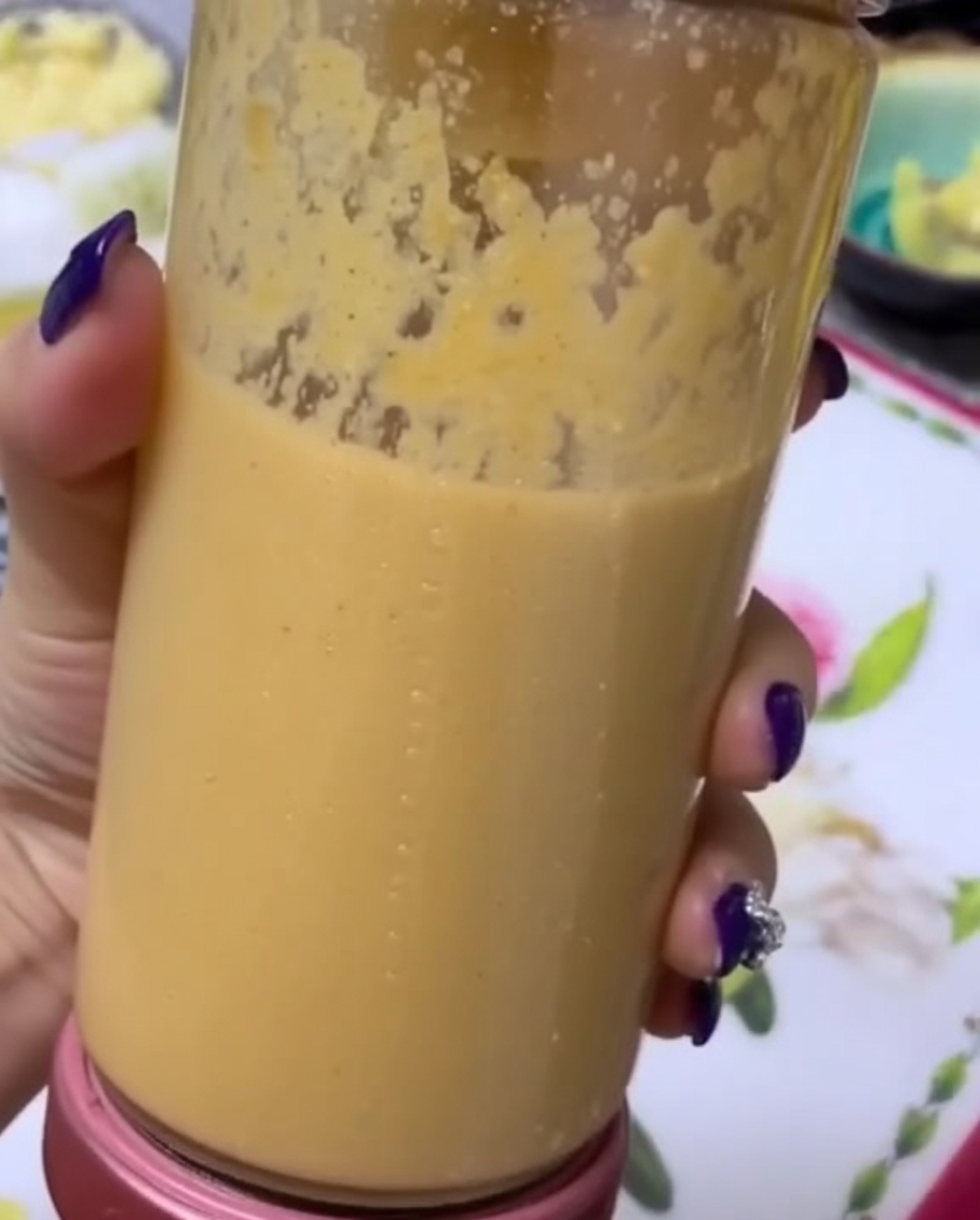 Una mano che tiene la caraffa trasparente di un frullatore piena di una purea di frutta e verdura liscia e densa.