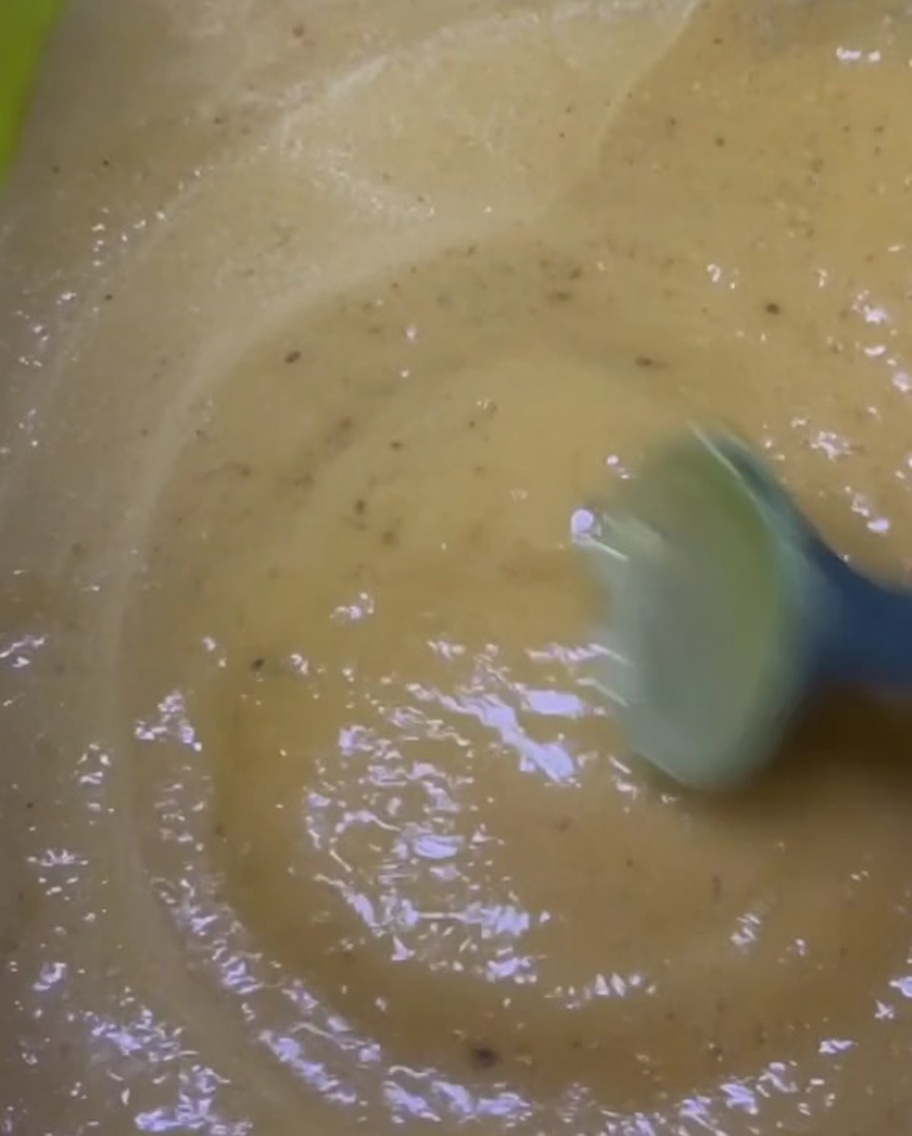 Una marinatura densa e giallo-marrone mescolata in una ciotola verde brillante.