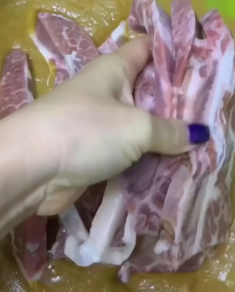 Una mano che immerge pezzi di costine di manzo crude in una densa marinatura frullata allinterno di una ciotola verde.