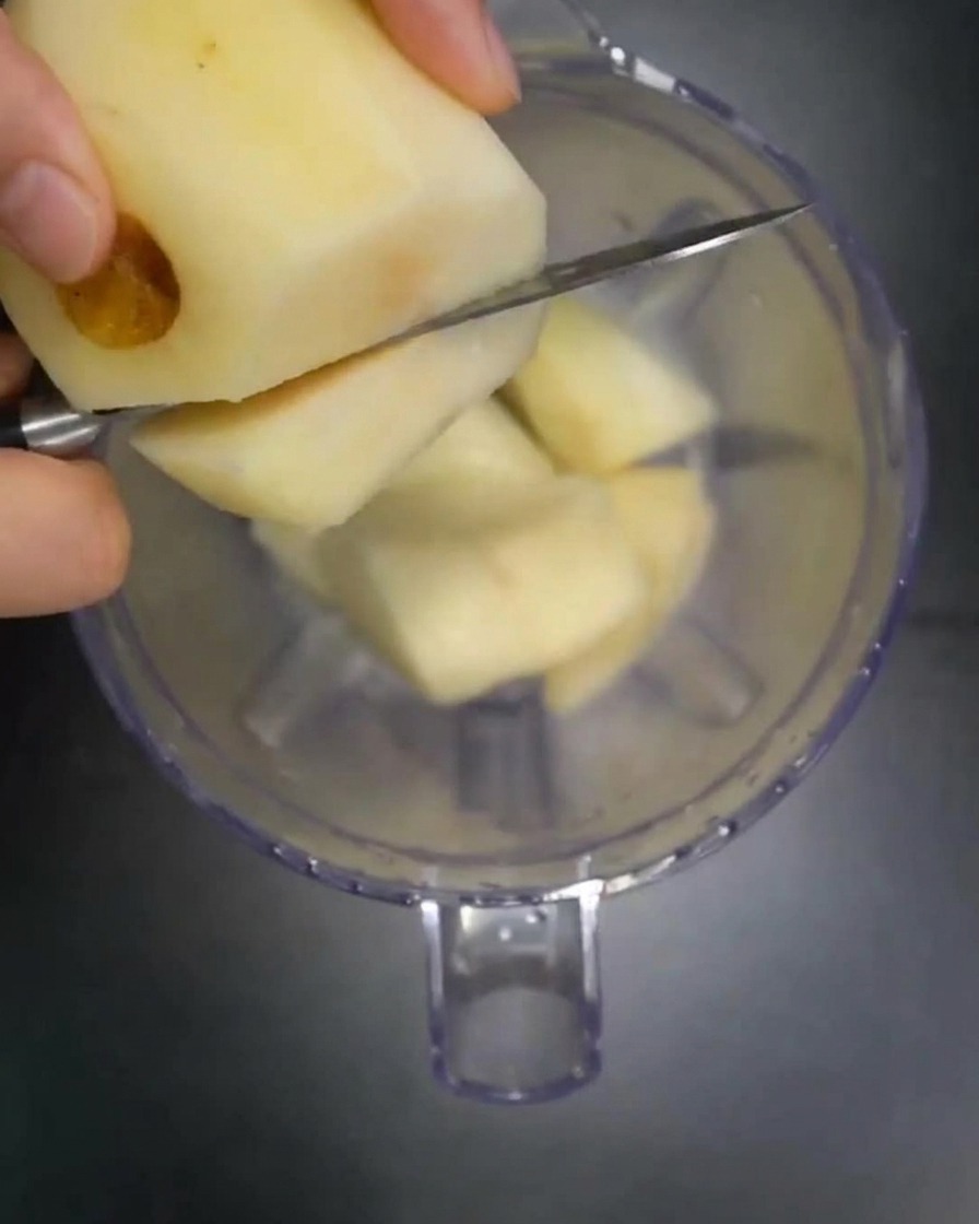 Pezzi di pera fresca, mela e cipolla aggiunti in un frullatore.